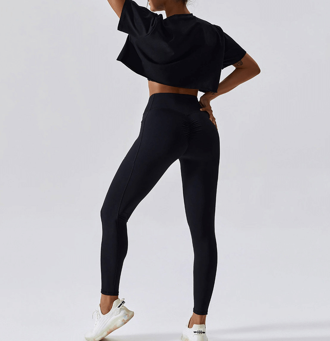 Woman wearing a black sports loose crop top and leggings, ideal for yoga, running, and gym activities. O-neckline, short sleeves.